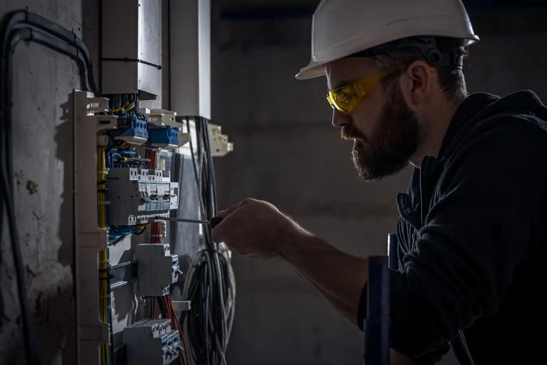 Técnico de capacete e óculos de proteção trabalhando em um quadro elétrico
